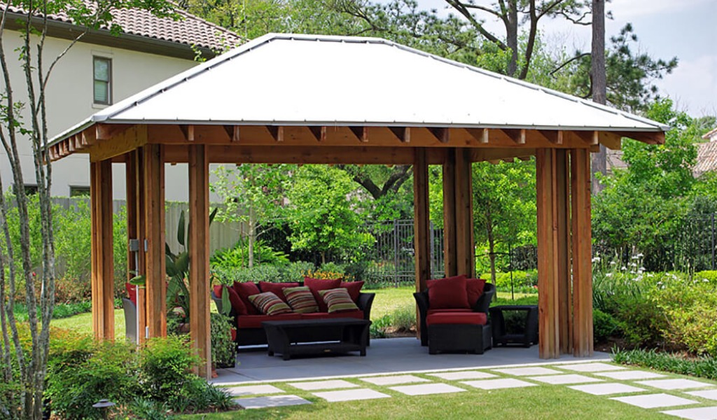 A backyard shade structure with closed roof covering outdoor furniture.