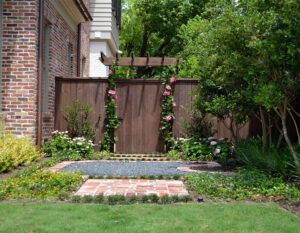 An arbor attached to a backyard fence with climbing vines and flowers.