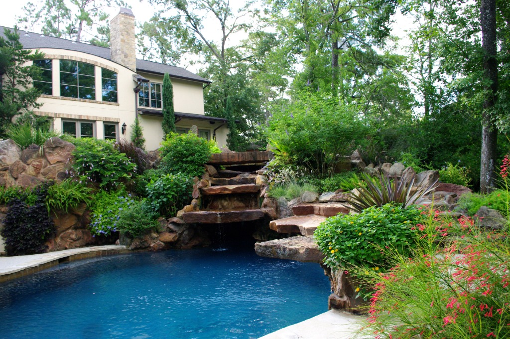 An outdoor pool with a beautiful garden and stone waterfall.