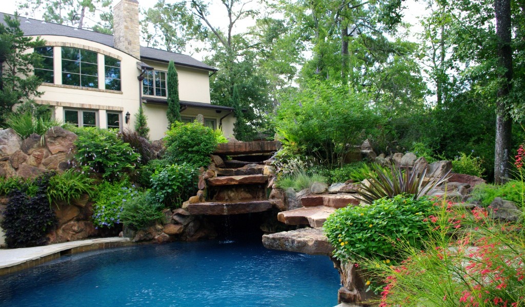 An outdoor pool with a beautiful garden and stone waterfall.